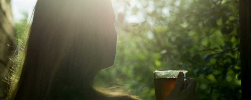 Mulher bebendo chá admirando raios de sol entre as árvores