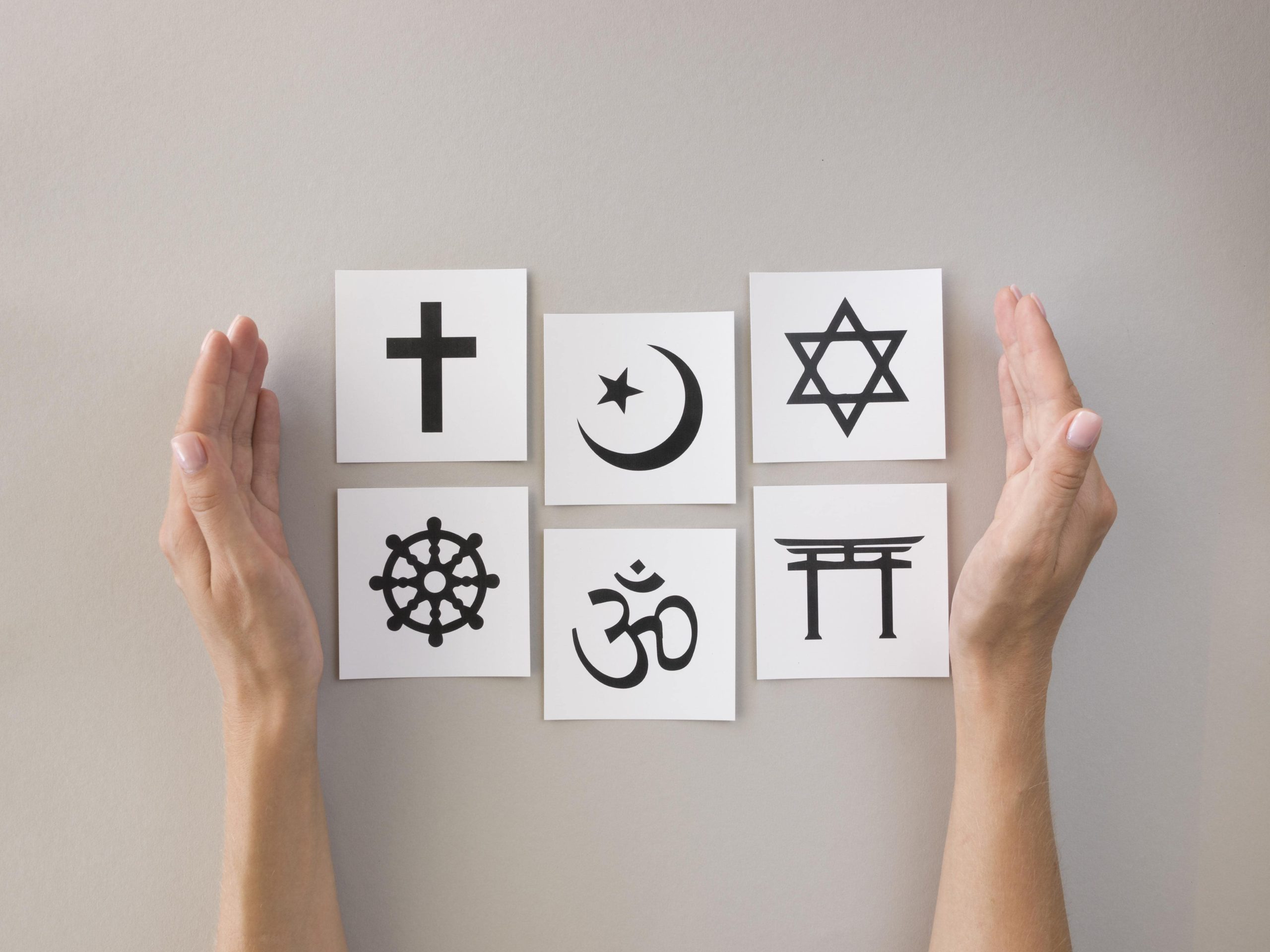 Mãos unem papéis com símbolos de religiões diversas - espiritualidade
